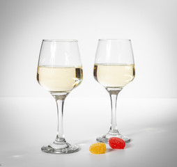 A glass of white wine. Multi-colored candies on a white background.
