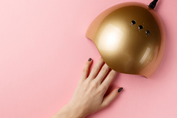Hand in UV lamp lights for nails on pink background. Top view. Flat lay. Copy space. Minimal...