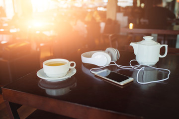 Smartphone, tea and headphones lying on desk in cafe, sun flare