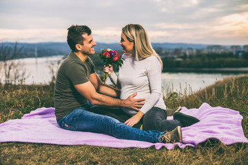 Husband giving flowers to his pregnant wife while enjoy spending time together outdoor.