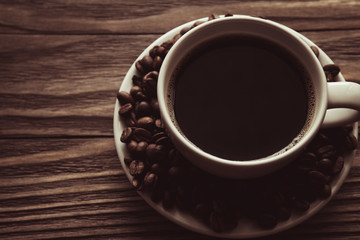 Cup of coffee, coffee beans on saucer on wooden background