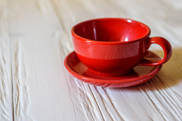 a red mug with a saucer on a white wooden background.