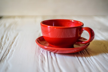 Fototapeta na wymiar a red mug with a saucer on a white wooden background.