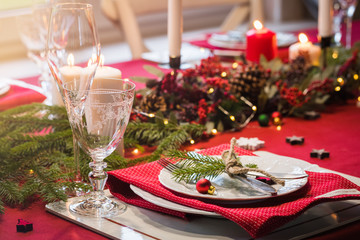 Table served for Christmas dinner, festive setting with decorations, burning candles and fir-tree...
