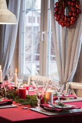 Table served for Christmas dinner, festive setting with decorations, burning candles and fir-tree branches