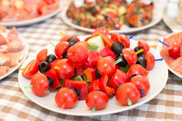 Set of tasty canape, on a plate of greens, tomatoes, peppers, cheese.