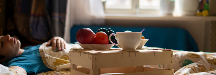morning breakfast food on the wooden tray in the hotel bed next to the sleeping person f