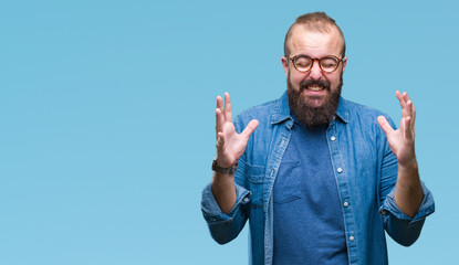 Young caucasian hipster man wearing glasses over isolated background crazy and mad shouting and yelling with aggressive expression and arms raised. Frustration concept.