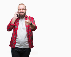 Young caucasian hipster man talking on smartphone over isolated background happy with big smile doing ok sign, thumb up with fingers, excellent sign