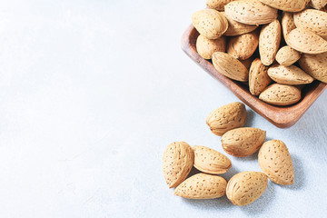Raw almond in the sinks in a wooden bowl on a white background, selective focus. The concept of healthy food.