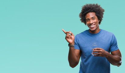 Afro american man drinking glass of water over isolated background very happy pointing with hand and finger to the side