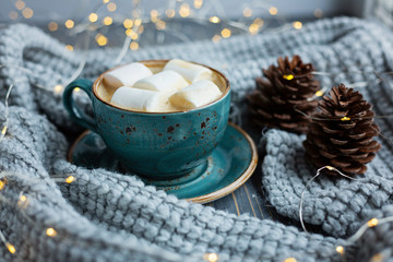 Obraz na płótnie Canvas Cup of coffee, marshmallow, warm knitted sweater on wooden background. Warm lights. Cozy winter morning.