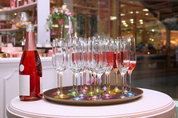 On the table are a lot of wine glasses with pink champagne and a bottle of wine