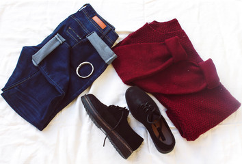 blue jeans, red oversize knitted sweater and black flat shoes, bracelet on white sheet. Overhead view of woman's casual day outfits. Trendy hipster look.