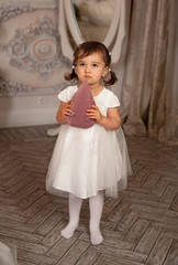 Little girl in white dress and flower is posing in a beautiful studio.