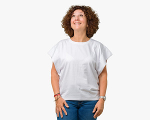 Beautiful middle ager senior woman wearing white t-shirt over isolated background smiling looking side and staring away thinking.