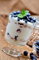 Greek yogurt with oatmeal, fresh blueberries and mint leaves full glass of oatmeals in background