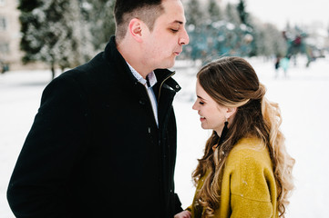 Young couple in love holding hands outdoor. Man and woman walk on a snowy winter park in love and leisure concept.