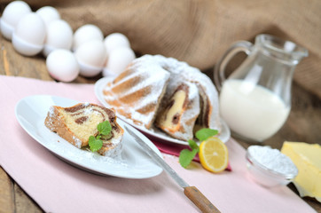 Cut of bundt cake sprinkled with sugar, lemon, melissa, milk, eggs and butter