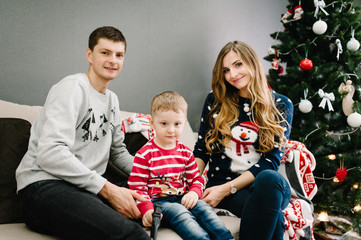 Happy family portrait, concept of a holiday. Mom, dad hugs son, sitting on the couch in home on the background of a Christmas tree. Happy New Year. Emotions of happiness. Close up.