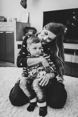 Portrait of happy mother and son celebrate Christmas. New Year's holidays. Toddler with mom in the festively decorated room with Christmas tree and decorations. Black and white photo.
