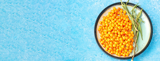 Sea-buckthorn berries in bowl and natural honey or sea buckthorn oil on blue background