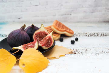 Slices of cut figs on a plate, cookies and berries on a bright blurry background, with yellow...