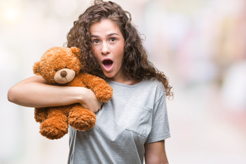 Young brunette girl holding teddy bear over isolated background scared in shock with a surprise face, afraid and excited with fear expression