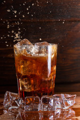 Glass still life image Cola with ice in a glass on a black wooden background