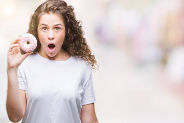 Young brunette girl eating donut over isolated background scared in shock with a surprise face, afraid and excited with fear expression