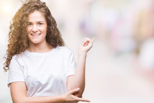 Beautiful brunette curly hair young girl wearing casual t-shirt over isolated background with a big smile on face, pointing with hand and finger to the side looking at the camera.