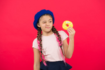Kid playful girl eat donut. Health and nutrition concept. Sweet life. Sweets shop and bakery concept. Kid fan of baked donuts. Delicious sweet donut. Girl in beret hat hold donut red background