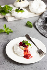 Mini Pavlova or meringue nests with whipped cream, berries and mint, selective focus. Grey concrete background. Copy space.
