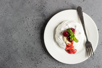 Mini Pavlova or meringue nests with whipped cream, berries and mint, selective focus. Grey concrete background. Copy space.