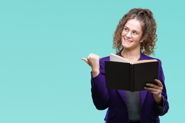 Young brunette student girl wearing school uniform reading a book over isolated background pointing and showing with thumb up to the side with happy face smiling