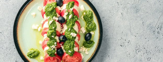 Tomato and mozzarella caprese salad and pesto sauce with olives on gray table. Food italian appetizer