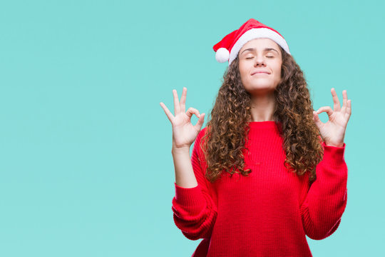 Young brunette girl wearing christmas hat over isolated background relax and smiling with eyes closed doing meditation gesture with fingers. Yoga concept.