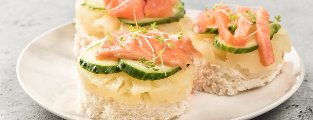 Bruschetta toast of white bread with slices of pineapple cucumber fish salmon and fresh green sprouts. Served on white plate on table. Top view flat lay with copy space