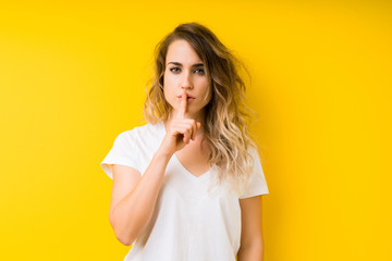 Young beautiful blonde woman over yellow background asking to be quiet with finger on lips. Silence and secret concept.