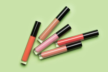 Five brightly coloured bottles of liquid lipstick and lip gloss randomly arranged on clean pastel green background shot with studio light from above