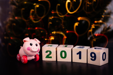 pink toy pig next to cubes on which is written in 2019 on the background of Christmas lights