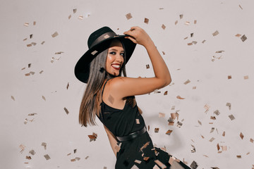 Cheerful brunette woman holding her hat and jumping over isolated background. Carefree girl...