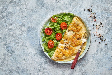 Classic egg omelette served with cherry tomato and arugula salad on side. Placed on white ceramic plate. Stone background with copy space.