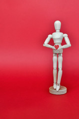 Bright concept for Valentine's day. Wooden model of a man holding a red heart on a red background.
