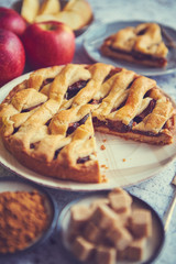 Delicious cutted apple pie cake with a fresh red and green apples fruits, brown and powder sugar. Placed on rusty scratched stone table.