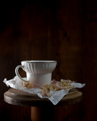 White porcelain cup with faded leaves of peony flowers at dark background, food photography