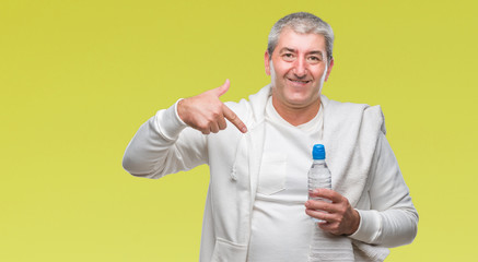 Handsome senior man training holding towel and water bottle over isolated background with surprise face pointing finger to himself