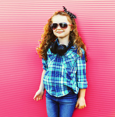 Fashion little girl child with wireless headphones on colorful pink wall background