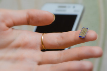 A girl holds the forefinger blue Nano SIM, smartphone in the background