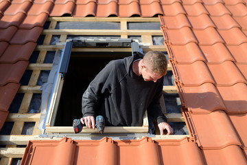 freundlicher Dachdecker Facharbeiter am Haus: Dachdecker Fenster einbauen im Eigenheim mit rotem...